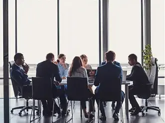 A group of people sitting at a table in front of windows.